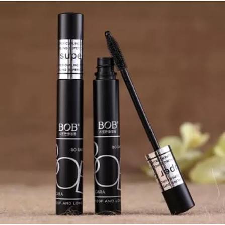 Three black BOB mascara tubes shown on a brown textured background, with one tube open and the wand resting diagonally against it.