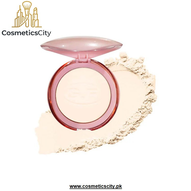 An open round compact of pressed powder in a translucent pink case, shown with a smear of the light beige powder behind it on a white background. The brand name 'CosmeticsCity' is visible in the top left corner.