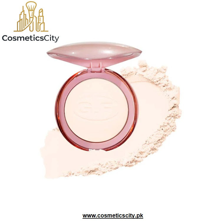 A round compact of pressed powder with a translucent pink lid and pink rim, shown open with a smear of the pale beige powder behind it on a white background. The brand name 'CosmeticsCity' is visible in the top left, and a website URL is visible at the bottom.