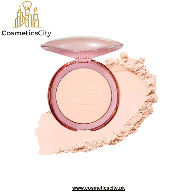 An open round makeup compact with a translucent pink lid and a light peach-beige pressed powder, shown with a smudge of matching powder on a white background. The brand name 'CosmeticsCity' appears in the top left, and a website URL is shown at the bottom.