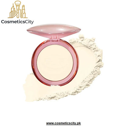 A round compact of pressed powder with a translucent pink lid and rim, shown open with a smear of the light beige powder behind it on a white background. The brand name 'CosmeticsCity' is visible in the top left corner.